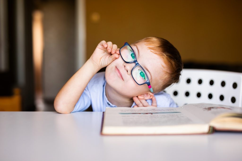 Cute toddler boy with down syndrome with big glasses reading interesting book.