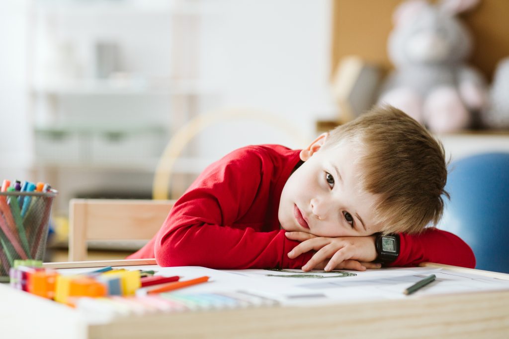 Sad little boy in red sweater feeling lonely and lying on a table, hate handwriting